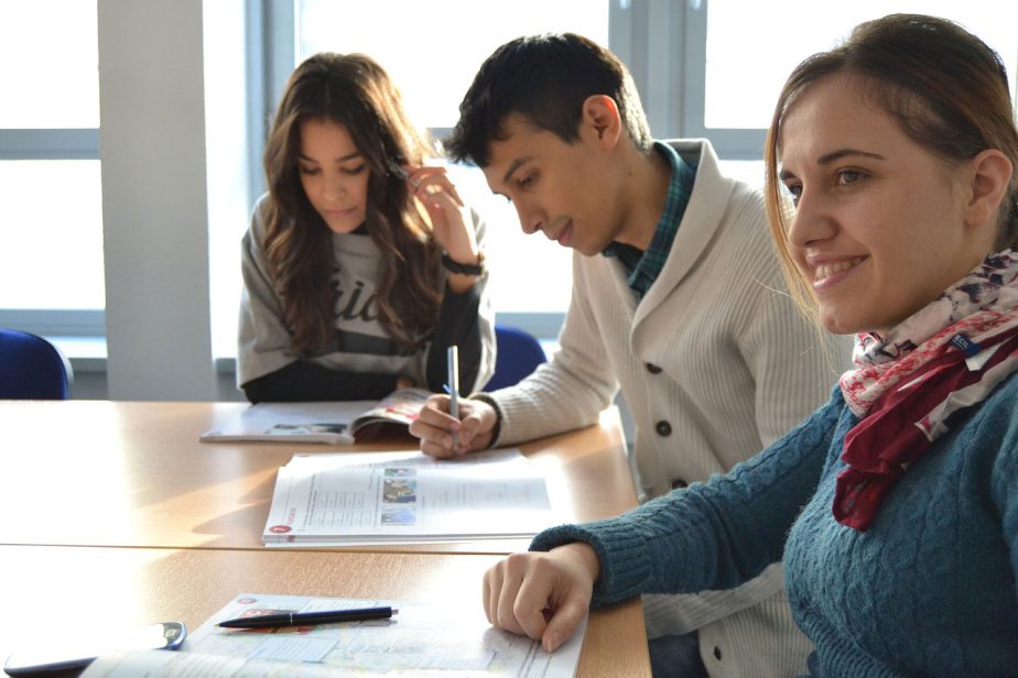 Trois jeunes adultes étudient autour d’une table avec des documents ouverts.