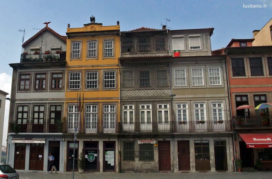 Façades d’immeubles mitoyens avec commerces au rez-de-chaussée, le long d’une rue.
