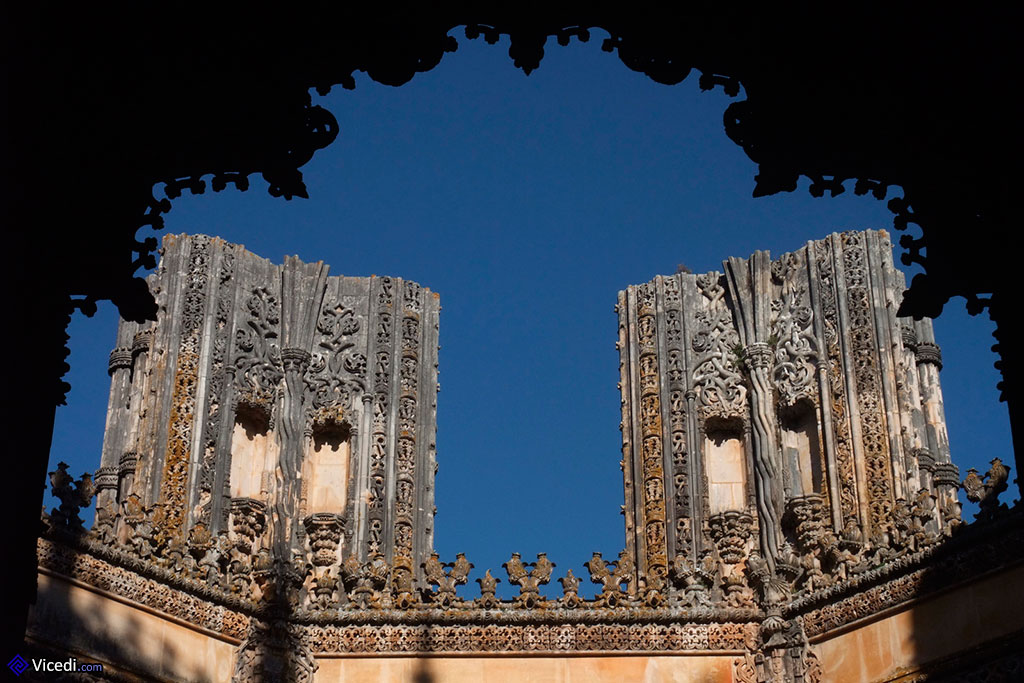 Vue sur deux des piliers inachevés, avec en ombre chinoise le portail principal Manuélin.