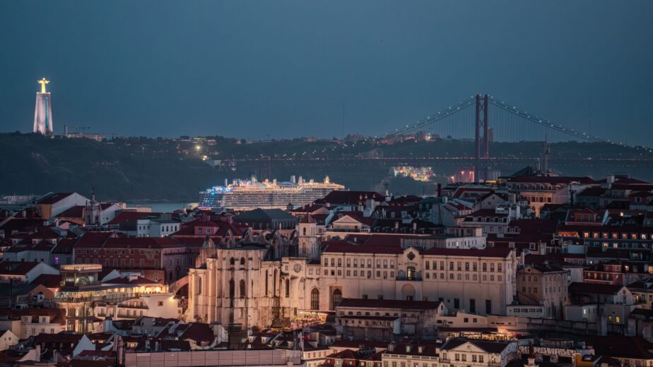 Vue nocturne sur les toits de Lisbonne, le pont du 25-Avril et une statue illuminée.