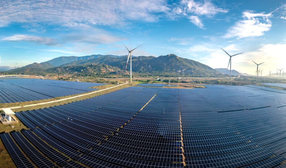 Un vaste champ de panneaux solaires avec plusieurs éoliennes à l’arrière-plan.