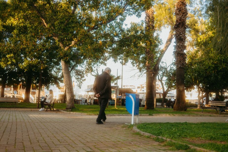 Une personne âgée marche dans un parc arboré, sur une allée pavée.