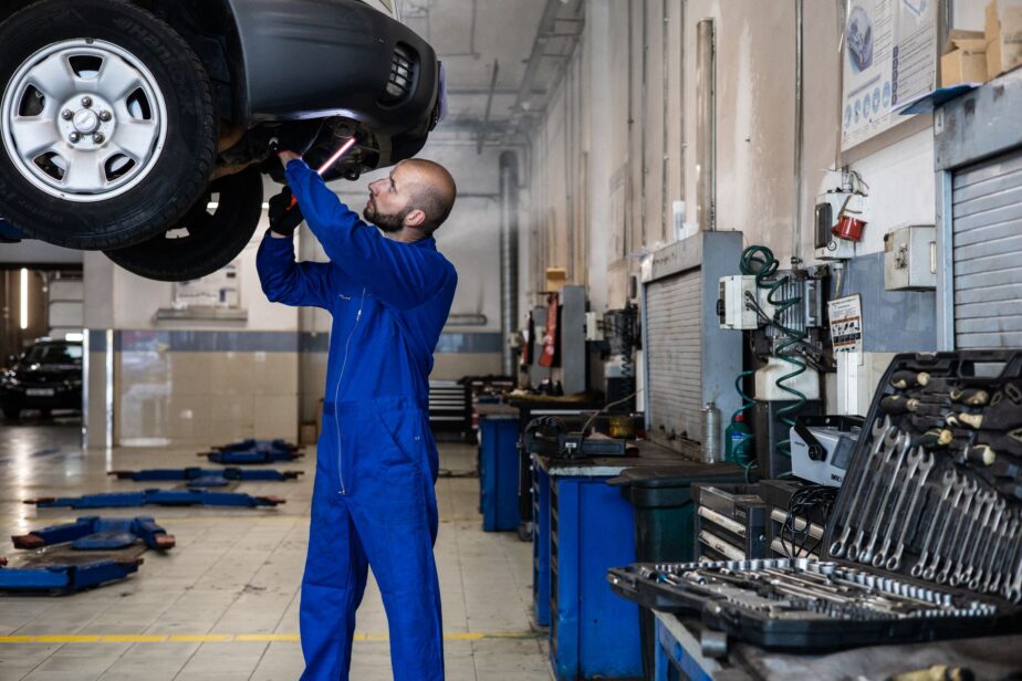 Un mécanicien examine le dessous d’une voiture surélevée dans un atelier.