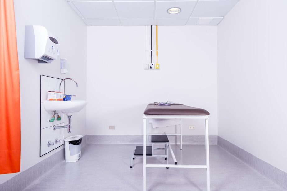 Salle d’examen médical vide, avec une table d’examen, un lavabo et un rideau orange.