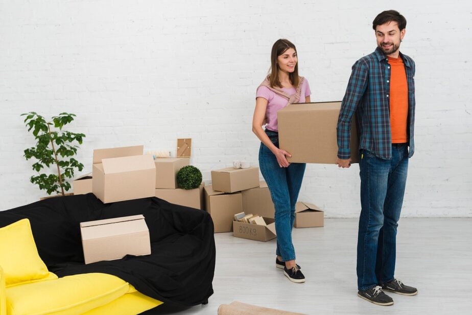 Un couple transporte un carton dans un logement où plusieurs cartons sont prêts.