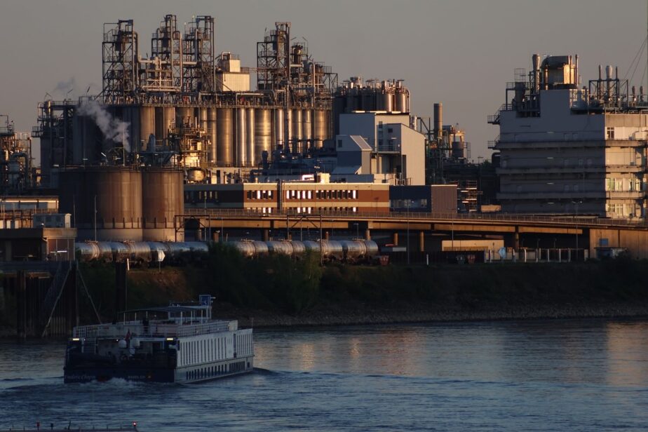 Complexe industriel avec de hautes structures métalliques au bord de l’eau et un bateau au premier plan.